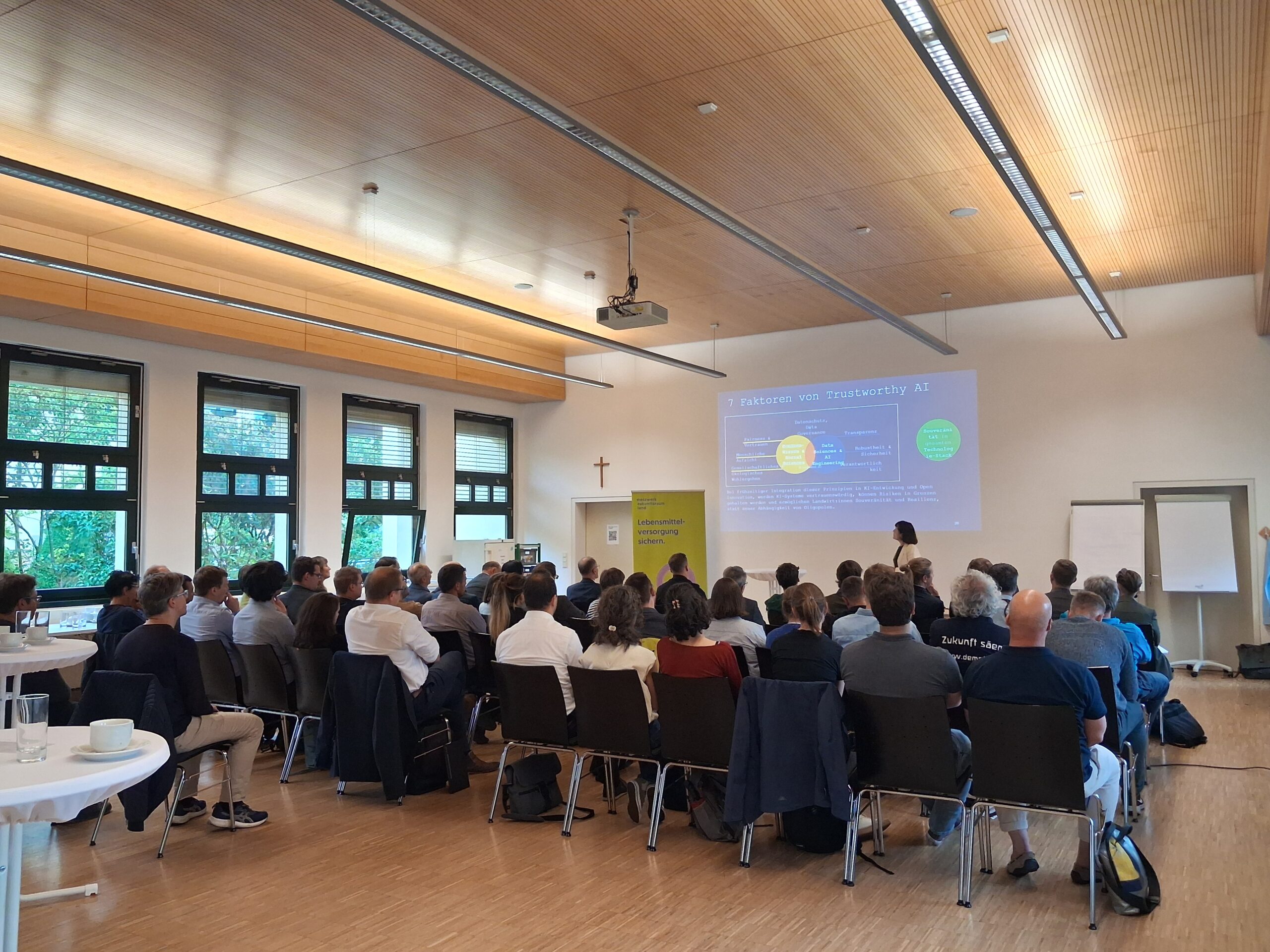 Menschen sitzen in einem Hörsaal. Man sieht sie nur von hinten