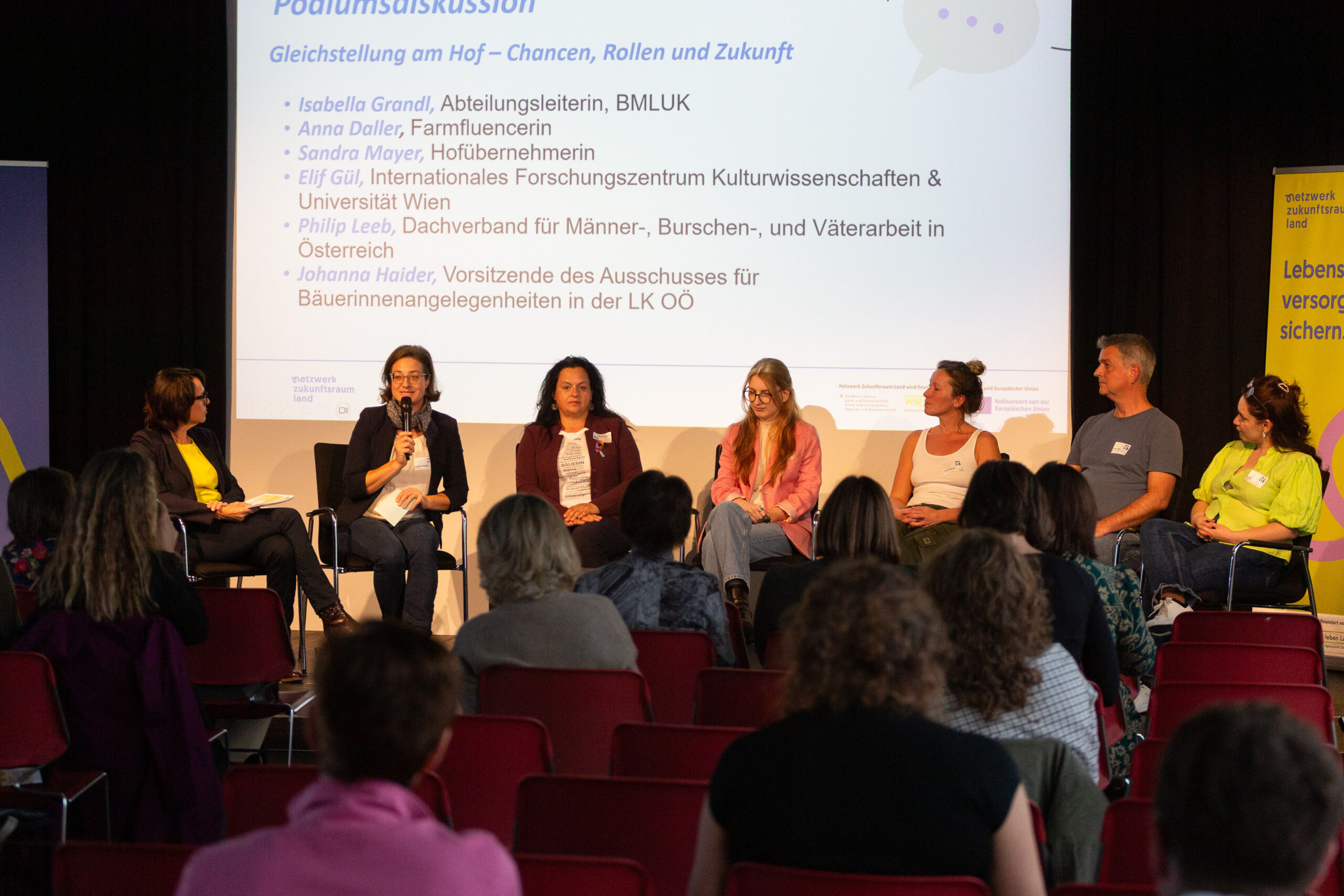 7 Menschen sitzen auf der Bühne und führen eine Podiumsdiskussion